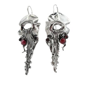 May include: Silver earrings with a unique, abstract design featuring red gemstone accents.