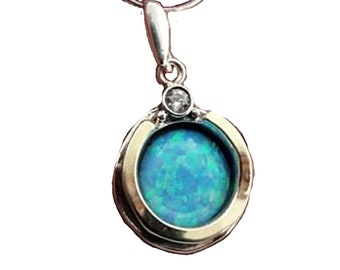 May include: A silver chain necklace with a round pendant featuring a blue opal stone set in a gold bezel. A small clear crystal accents the top of the pendant.