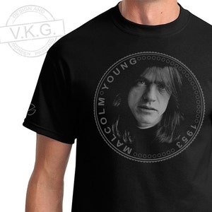 Puede incluir: Camiseta negra con un gráfico circular de Malcolm Young, un músico, con el texto "Malcolm Young 1953 - 2017" alrededor de la imagen.