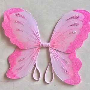 May include: Pink butterfly wings with glitter accents. The wings are made of a sheer fabric and have a pink and white ombre effect.
