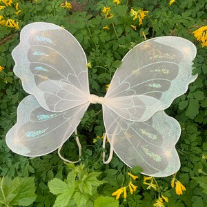 Op de afbeelding: Witte fee&euml;nvleugels met iriserende glitteraccenten. De vleugels zijn gemaakt van een dunne, delicate stof en perfect om een ​​toets van magie toe te voegen aan elk kostuum.