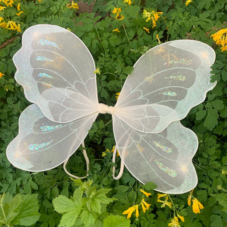 Op de afbeelding: Witte fee&euml;nvleugels met iriserende glitteraccenten. De vleugels zijn gemaakt van een dunne, delicate stof en perfect om een ​​toets van magie toe te voegen aan elk kostuum.