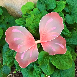 May include: Pink butterfly wings with glitter accents. The wings are made of sheer fabric and are perfect for a costume or party.