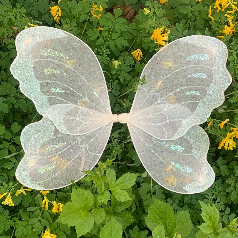 Op de afbeelding: Witte fee&euml;nvleugels met iriserende glitteraccenten. De vleugels zijn gemaakt van een dunne, delicate stof en hebben een gegolfde rand.
