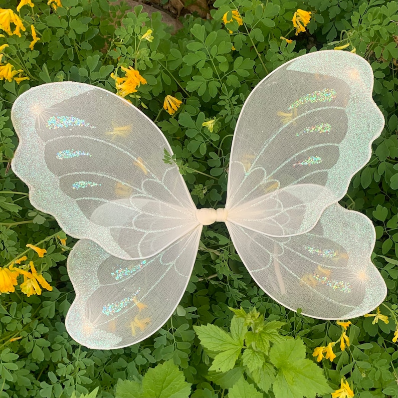 Op de afbeelding: Witte fee&euml;nvleugels met iriserende glitteraccenten. De vleugels zijn gemaakt van een dunne, delicate stof en perfect om een ​​toets van magie toe te voegen aan elk kostuum.