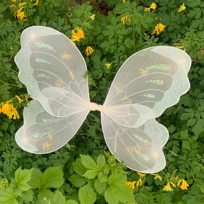 Op de afbeelding: Witte fee&euml;nvleugels met iriserende glitteraccenten. De vleugels zijn gemaakt van een dunne, delicate stof en perfect om een ​​toets van magie toe te voegen aan elk kostuum.