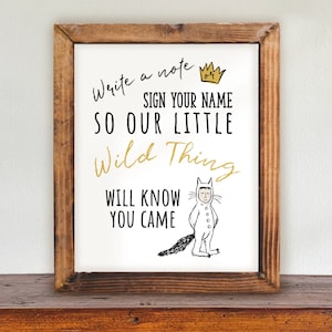 May include: A white sign with a brown wood frame, featuring a black and white illustration of a character from the book Where the Wild Things Are. The sign reads "Write a note, sign your name, so our little wild thing will know you came."