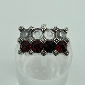 May include: A silver ring with a rectangular design featuring red and clear rhinestones set in a silver frame.