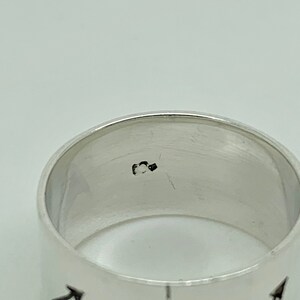 May include: Silver band ring with a black inscription on the inside of the band. The inscription is a small number.