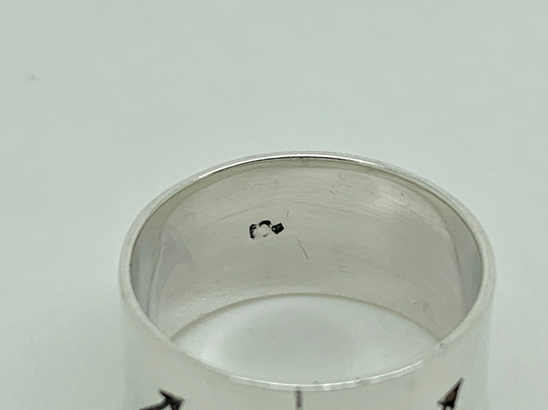 May include: Silver band ring with a black inscription on the inside of the band. The inscription is a small number.
