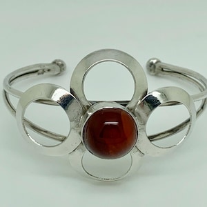 May include: A silver bracelet with a red carnelian stone set in the centre. The bracelet is made of four interlocking circles.