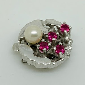 May include: A silver clasp featuring a pearl and five pink gemstones. The clasp is designed in a floral pattern.