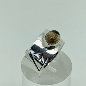 May include: A silver ring with a geometric design and a clear, oval-shaped gemstone.