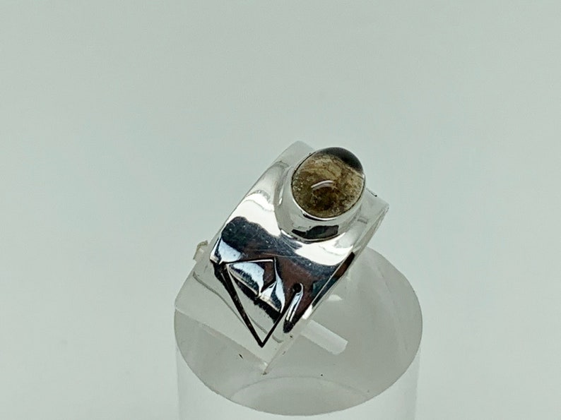 May include: A silver ring with a geometric design and a clear, oval-shaped gemstone.
