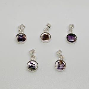 May include: Five circular silver pendants, each featuring a small, polished stone with deep purple and white banding. Every pendant includes a silver bail at the top for attachment, arranged in a group of three on top and two on the bottom.