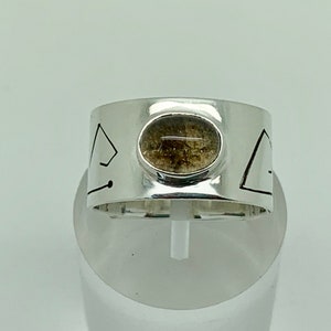 May include: A silver ring with a geometric design and a brown stone set in the center.