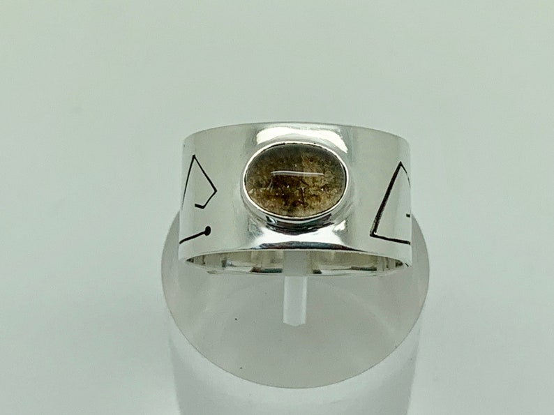 May include: A silver ring with a geometric design and a brown stone set in the center.
