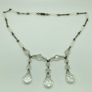 May include: A vintage crystal necklace with a delicate chain and three teardrop-shaped pendants. The necklace is made of clear glass beads and has a silver-toned metal clasp.