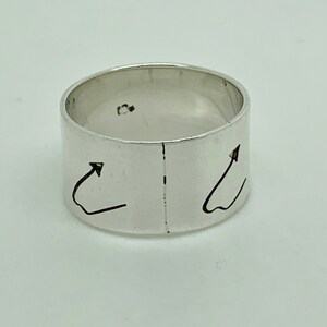 May include: A silver ring with two arrows pointing upwards on the band.
