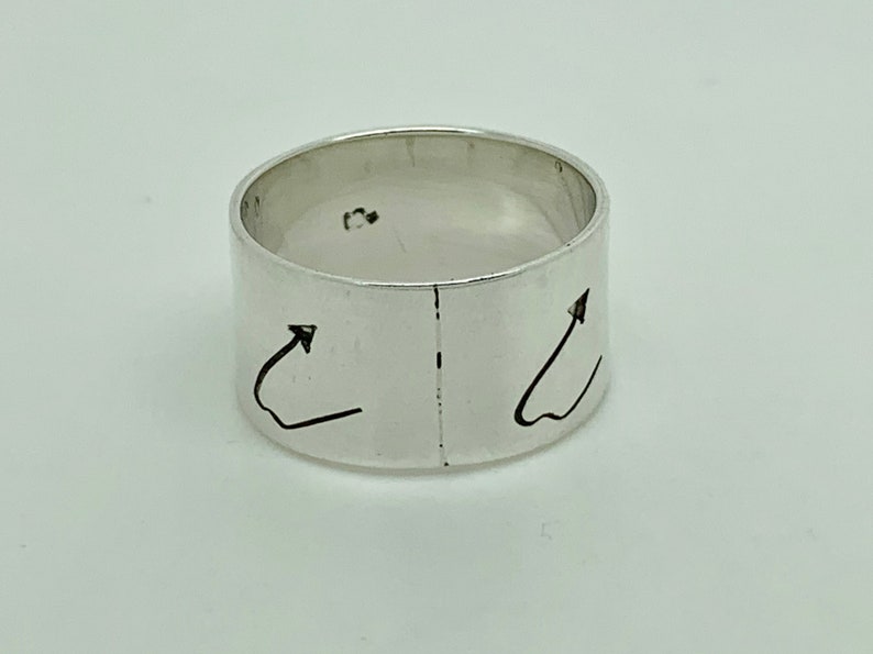 May include: A silver ring with two arrows pointing upwards on the band.