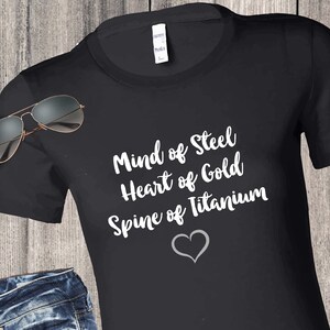 May include: Black t-shirt with white text that reads "Mind of Steel, Heart of Gold, Spine of Titanium" with a white heart symbol below the text.