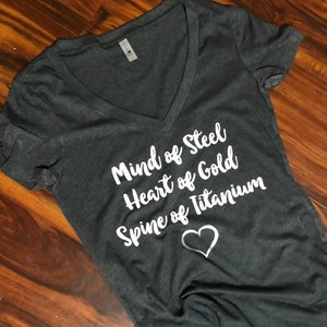 May include: A dark grey V-neck t-shirt with the text "Mind of Steel, Heart of Gold, Spine of Titanium" in white lettering and a white heart.