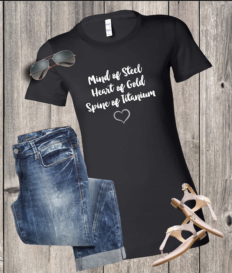 May include: Black t-shirt with white text that reads "Mind of Steel, Heart of Gold, Spine of Titanium" with a white heart symbol below the text.