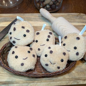 Peut inclure: Cinq biscuits en peluche marrons aux pépites de chocolat avec des visages souriants et des pépites de chocolat. Les biscuits sont dans un panier tissé sur une surface en bois.