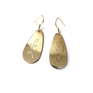May include: Gold-toned dangle earrings featuring a leaf design. The earrings are oval-shaped and have a simple, minimalist style.