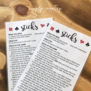 May include: Two white cards with the game "sticks" printed in black script. The cards include game rules, objectives, and instructions. The top of the cards have suit symbols in red and black.