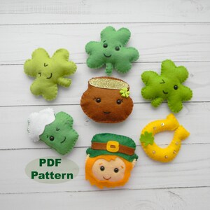 May include: A set of felt ornaments with a St. Patrick's Day theme. The ornaments include a pot of gold, a horseshoe, a leprechaun, and several shamrocks. The ornaments are all green, yellow, and brown.