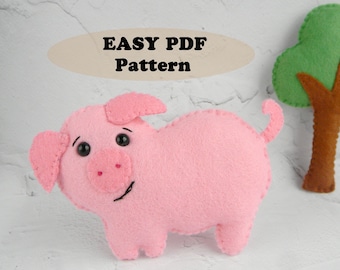 May include: A pink felt pig with black eyes and a brown felt tree. The text "EASY PDF Pattern" is on a tan oval shape. The text "*Magic Pattern Shop*" is at the bottom of the image.