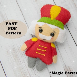 May include: A felt toy pattern for a Nutcracker soldier. The pattern includes a red and green uniform, a white beard, and a yellow hat. The pattern is labeled "Easy PDF Pattern".