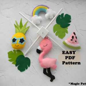 May include: A felt mobile with a yellow pineapple wearing sunglasses, a rainbow, a pink flamingo, a watermelon slice, and green leaves. The mobile hangs from a white wooden frame. The image includes the text "EASY PDF Pattern".