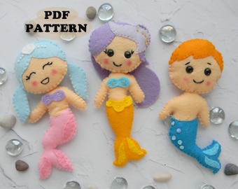 May include: Three felt mermaid dolls, one with purple hair, one with blue hair, and one with orange hair. The dolls are all smiling and have large eyes. The dolls are wearing mermaid tails and have seashells on their heads.