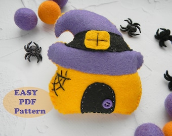 May include: A felt witch's house ornament with a purple hat, yellow walls, and a black door. The ornament is surrounded by felt balls and plastic spiders.
