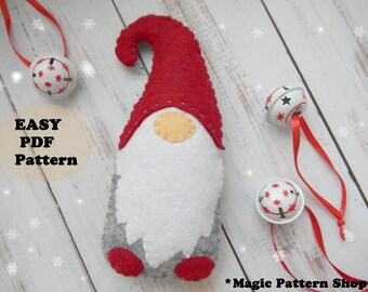 May include: A felt gnome ornament with a red hat, white beard, and grey legs. The gnome is on a white wooden background with red and white jingle bells.