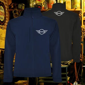 May include: Two softshell jackets, one navy blue and one black, are displayed. Each jacket features a white "MINI" logo on the chest and back. The jackets have a full zipper and a stand-up collar, suitable for cooler weather.