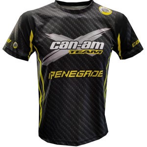 Puede incluir: Camiseta negra y amarilla Can-Am Team Renegade. La camiseta tiene un patrón de fibra de carbono con el logotipo de Can-Am en blanco y gris en el pecho. Los detalles amarillos están en los laterales y las mangas. La palabra "RENEGADE" es amarilla.