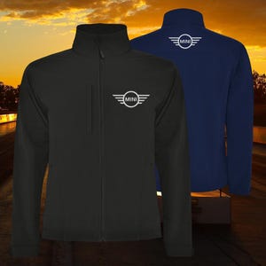 May include: Black and navy blue softshell jackets with the white "MINI" logo on the chest and back. The jackets have a full-zip closure, a stand-up collar, and a small chest pocket. The background is a sunset.