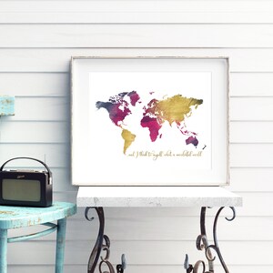 Può includere: Una stampa artistica incorniciata di una mappa del mondo con un design ad acquerello nei toni dell'oro, magenta e viola. La stampa include il testo "and I think to myself what a wonderful world". La stampa è esposta su un tavolo bianco.