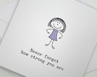 May include: A square white greeting card featuring a black line drawing of a stick figure with a bob haircut wearing a light purple dress. Below the figure, the text reads: Never forget how strong you are. The card is placed on a white envelope.