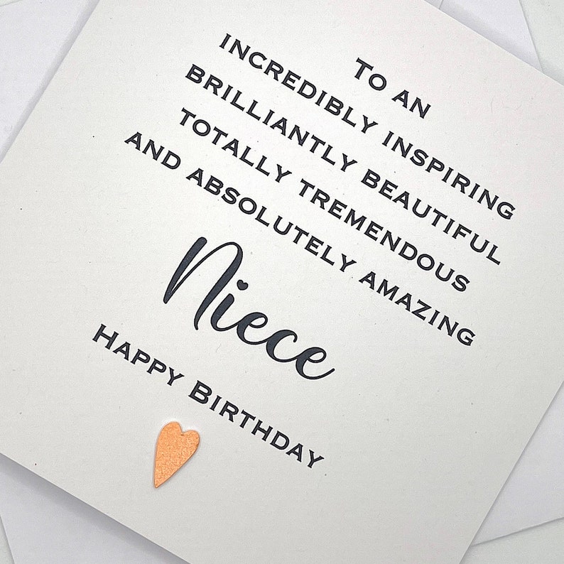 Puede incluir: Una tarjeta blanca con texto negro que dice "To an incredibly inspiring brilliantly beautiful totally tremendous and absolutely amazing Niece Happy Birthday". Un peque&ntilde;o coraz&oacute;n dorado se encuentra en la esquina inferior derecha.