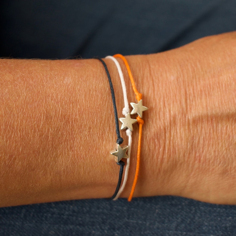May include: Three bracelets with silver star charms. The bracelets are black, white, and orange.