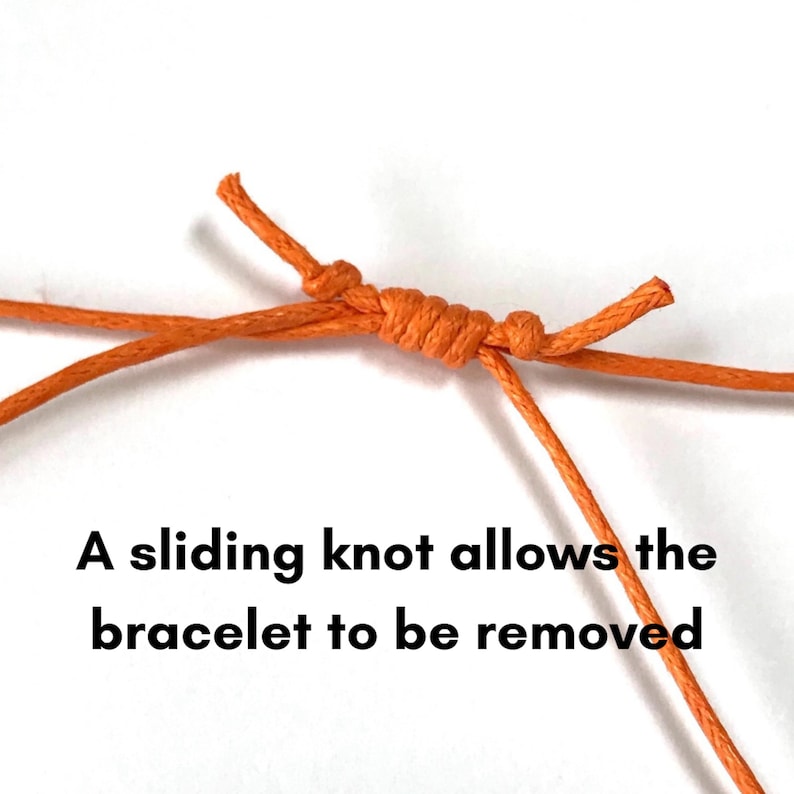 May include: A close-up of an orange cord bracelet with a sliding knot. The text "A sliding knot allows the bracelet to be removed" is written below the bracelet.