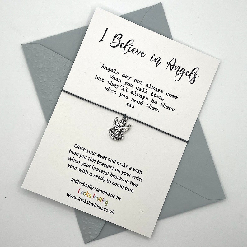 May include: A white card with black text that reads "I Believe in Angels" and a quote about angels. The card is attached to a black string with a silver angel charm. The card also includes instructions for making a wish and the text "Individually Handmade by Looks Inviting www.looksinviting.co.uk".