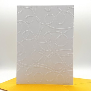 Peut inclure: Une carte de vœux blanche avec un motif abstrait en relief de lignes et de boucles tourbillonnantes. La carte est rectangulaire et a une surface texturée. Une enveloppe jaune est visible dans le coin inférieur.