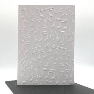 May include: A white card featuring an embossed design of musical notes, treble clefs, and other musical symbols. The card has a textured surface and a simple, elegant design, suitable for music enthusiasts.