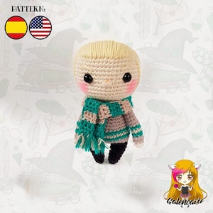 Puede incluir: Muñeca amigurumi de crochet con cabello rubio, vistiendo un suéter a rayas gris y verde y una bufanda verde. La muñeca tiene mejillas sonrosadas y ojos negros.