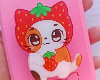 Può includere: Una custodia per telefono rosa con un gatto bianco che indossa un costume di fragola rossa e tiene una fragola rossa. Il gatto ha le orecchie arancioni e un viso bianco con baffi neri.